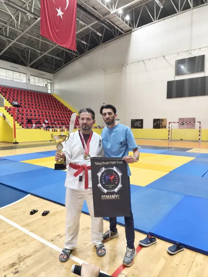Kupa ve madalyasıyla antrenör, elinde Yakup Demir Fight Team flaması